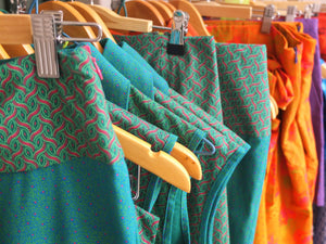 Bunte Kleider, Röcke, Hosen in grün und orange auf Kleiderbügel